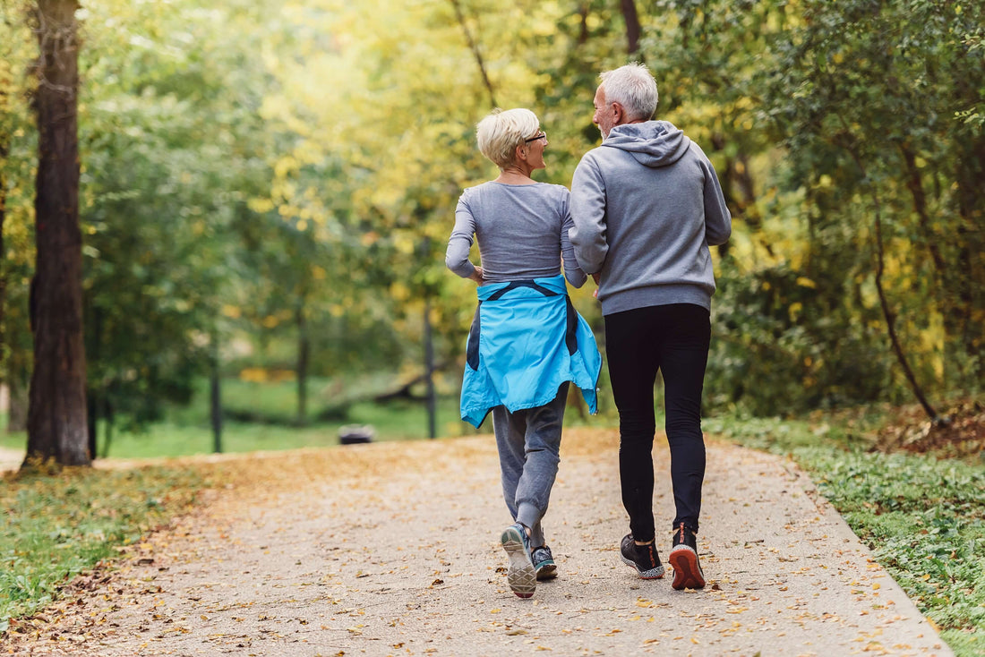 Two older adults walk along a trail.