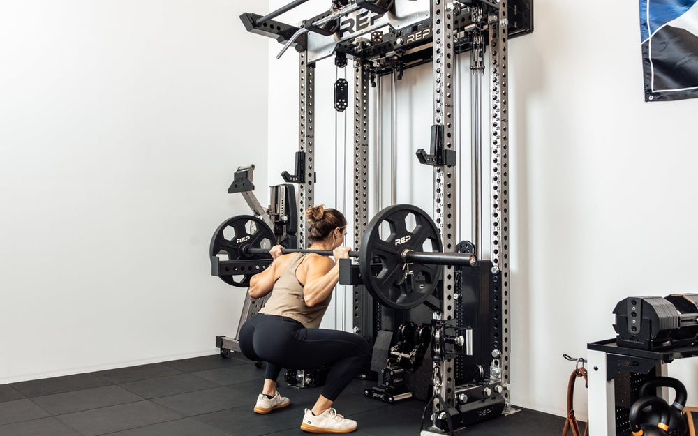An athlete performing barbell squats off the front of the Wall-Mounted Ares™ 2.0 with spotter arms